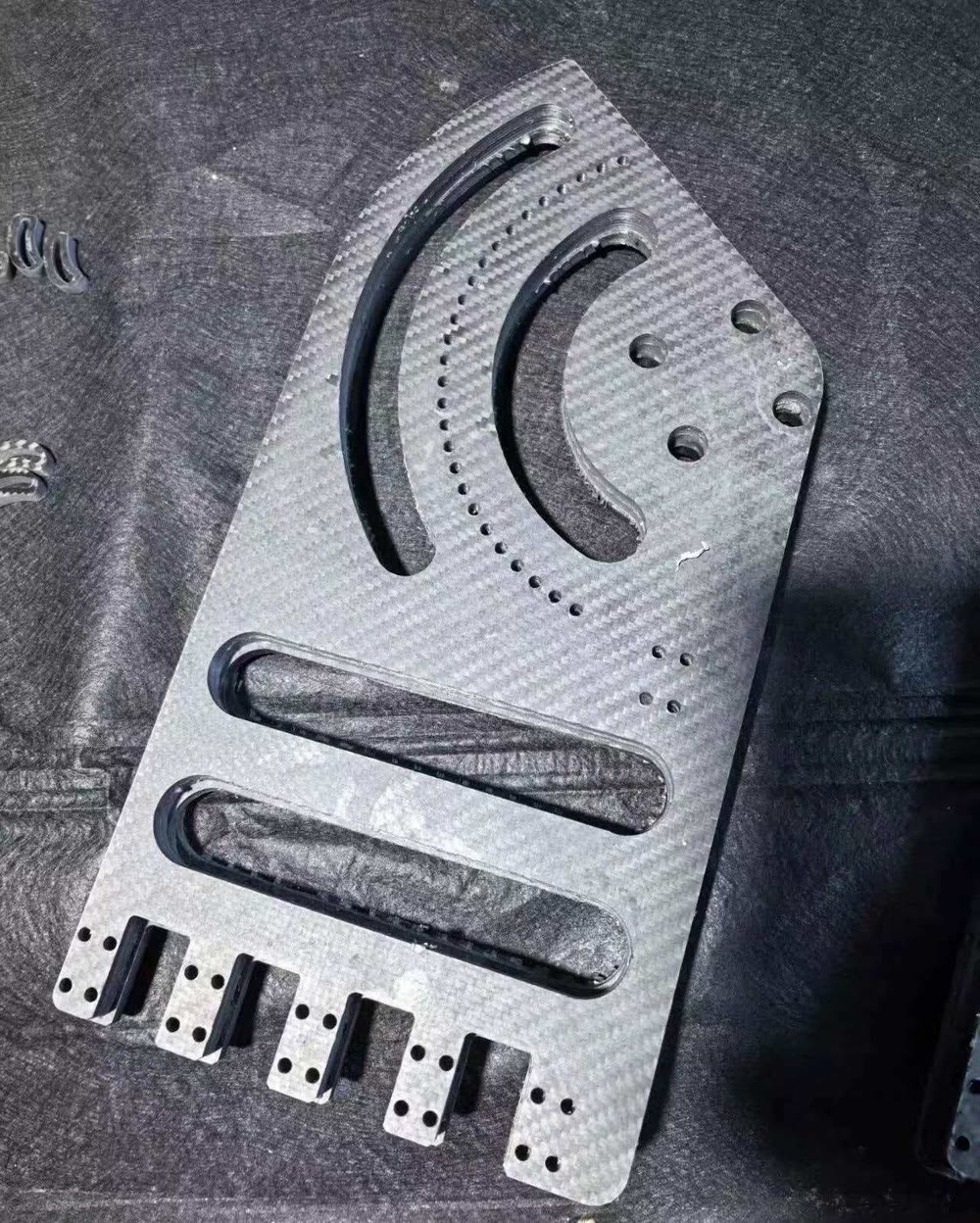 Close view of a machined carbon fiber sheet part showing slots, small holes and layered edges